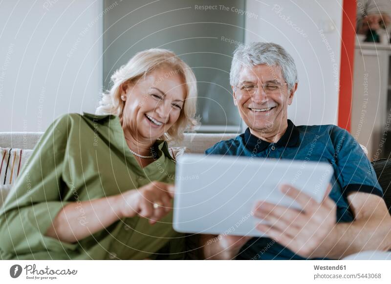 Glückliches älteres Ehepaar sitzt zu Hause auf der Couch und teilt sich ein Tablet lachen Tablet Computer Tablet-PC Tablet PC iPad Tablet-Computer Senior