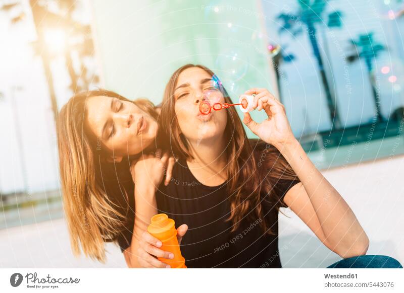 Zwei glückliche junge Frauen, die Seifenblasen pusten Spaß Spass Späße spassig Spässe spaßig Freundinnen Freunde Freundschaft Kameradschaft weiblich Erwachsener