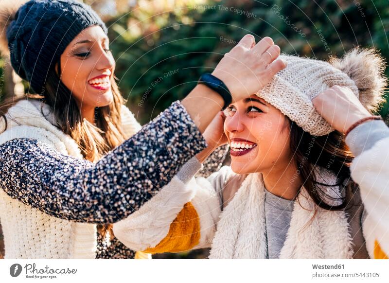Zwei hübsche Frauen amüsieren sich mit Wollmützen Spaß Spass Späße spassig Spässe spaßig Mütze Mützen Freundinnen weiblich schön Strickmütze Strickmützen