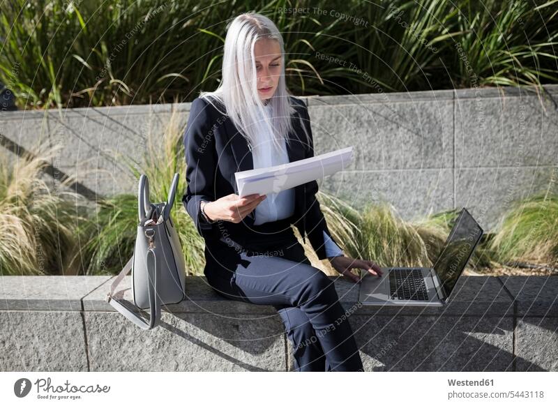 Junge Geschäftsfrau sitzt in der Stadt mit Dokumenten und Laptop an einer Wand sitzen sitzend Notebook Laptops Notebooks Frau weiblich Frauen Geschäftsfrauen