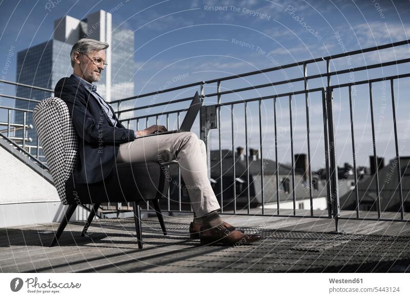 Grauhaariger Geschäftsmann sitzt mit Laptop auf dem Balkon Notebook Laptops Notebooks Businessmann Businessmänner Geschäftsmänner sitzen sitzend Computer