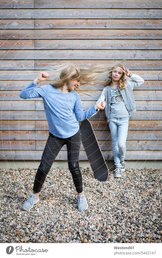 Zwei Mädchen mit Skateboard vor Holzfassade Hausfassade Fassade hölzern weiblich Rollbretter Skateboards Gebäudefront Fassaden hoelzern Kind Kinder Kids Mensch