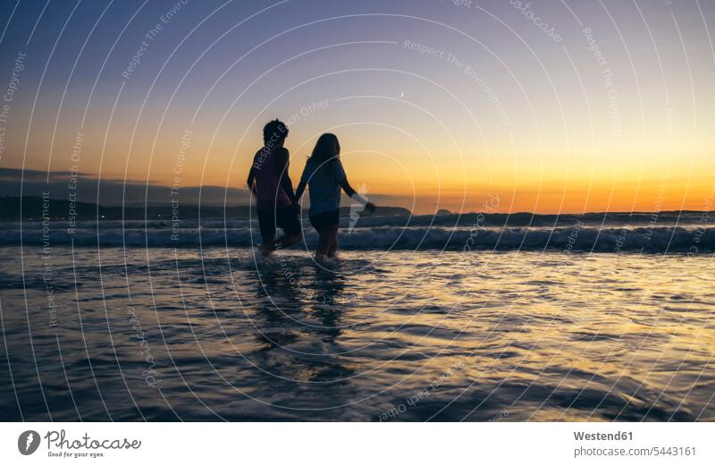 Junges Paar beim Spaziergang im Meer in der Abenddämmerung Meere Pärchen Paare Partnerschaft Gewässer Wasser Mensch Menschen Leute People Personen gehen gehend