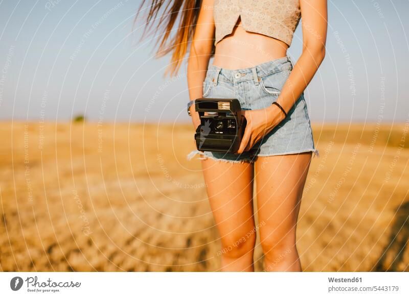 Junge Frau mit Sofortbildkamera auf einem Feld bei Sonnenuntergang, Teilansicht weiblich Frauen Polaroid-Kamera Erwachsener erwachsen Mensch Menschen Leute