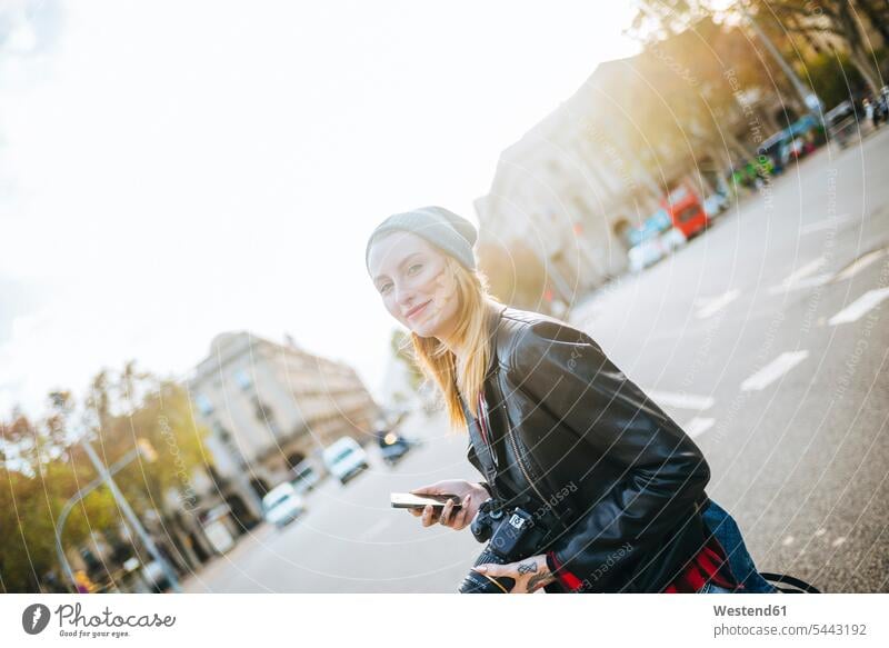 Spanien, Barcelona, lächelnde junge Frau mit Mobiltelefon auf der Straße weiblich Frauen Portrait Porträts Portraits Erwachsener erwachsen Mensch Menschen Leute