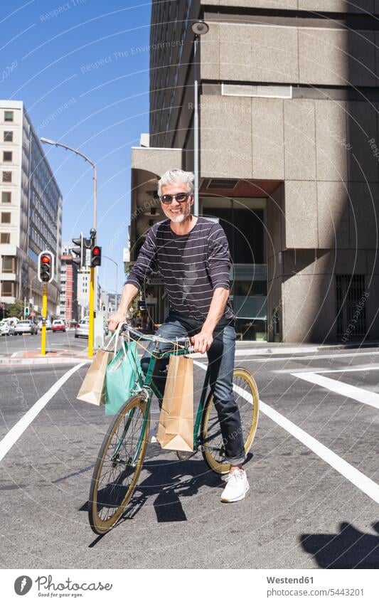 Älterer Mann fährt Fahrrad in der Stadt Bikes Fahrräder Räder Rad lächeln Einkaufstasche Einkaufstaschen unterwegs auf Achse in Bewegung staedtisch städtisch