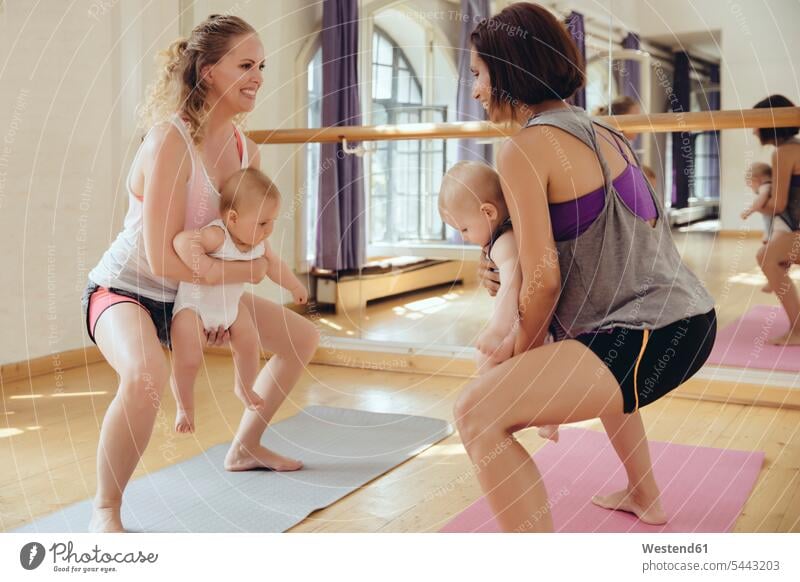Zwei Mütter beim Training auf Yogamatten mit Babys im Arm Mutter Mami Mutti Mama trainieren lächeln Babies Säuglinge Kind Kinder Spaß Spass Späße spassig Spässe