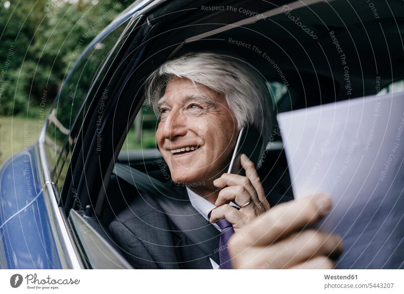 Lächelnder Senior-Geschäftsmann mit Dokumenten am Telefon im Auto telefonieren anrufen Anruf telephonieren Businessmann Businessmänner Geschäftsmänner Wagen