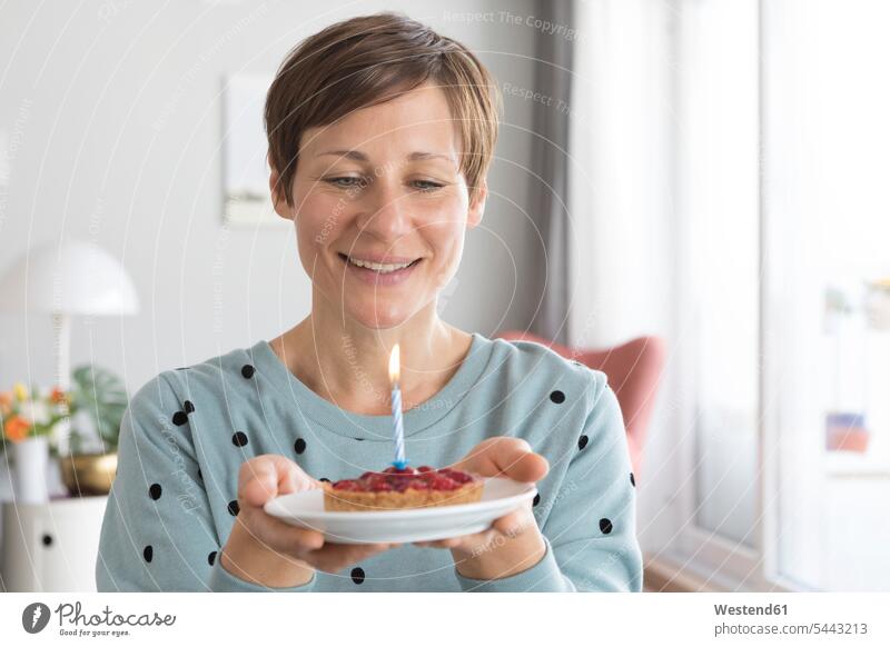 Porträt einer lächelnden Frau, die einen Teller mit Geburtstagskuchen hält Portrait Porträts Portraits Geburtstagstorten weiblich Frauen Torte Torten Kuchen