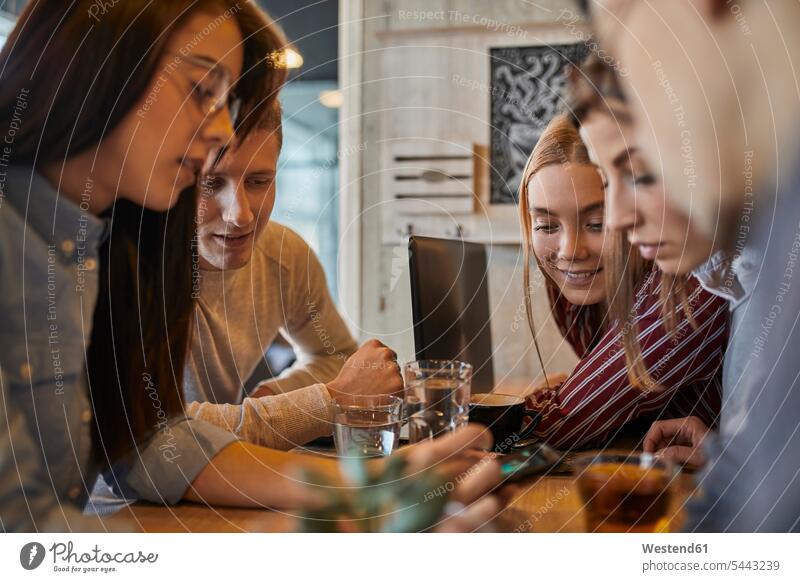 Gruppe von Freunden sitzt zusammen in einem Café und teilt sich ein Smartphone Gemeinsam Zusammen Miteinander iPhone Smartphones Cafe Kaffeehaus Bistro Cafes