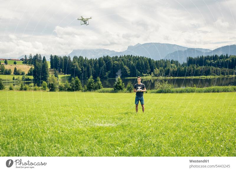 Deutschland, Bayern, Pfronten, junger Mann fliegt mit seiner Drohne am Seeufer Aussicht Ausblick Ansicht Überblick Drohnen Männer männlich stehen stehend steht