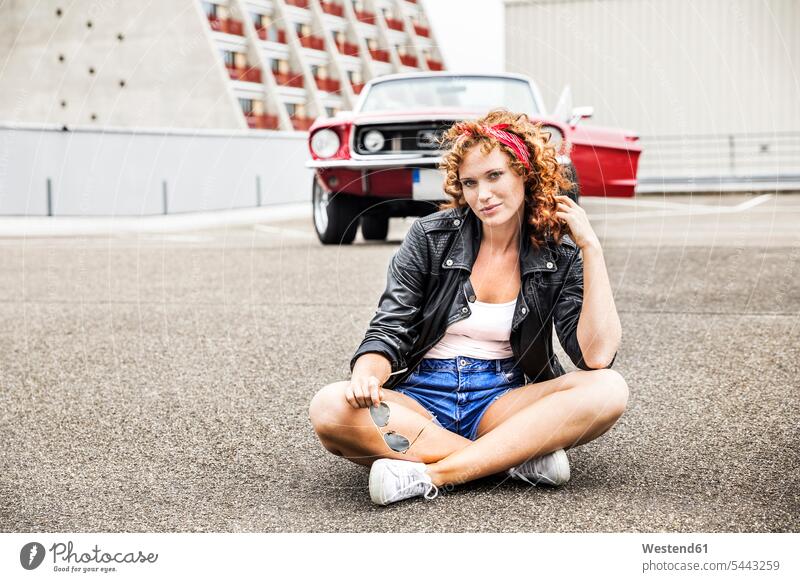 Porträt einer selbstbewussten rothaarigen Frau, die auf dem Parkdeck sitzt Portrait Porträts Portraits sitzen sitzend Auto Wagen PKWs Automobil Autos weiblich