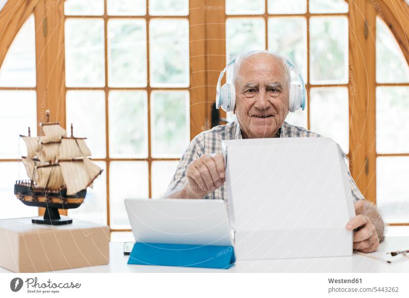 Porträt eines selbstbewussten älteren Mannes mit Kopfhörern mit Tablette, Schiffsmodell und Verpackung auf dem Tisch Tablet Computer Tablet-PC Tablet PC iPad