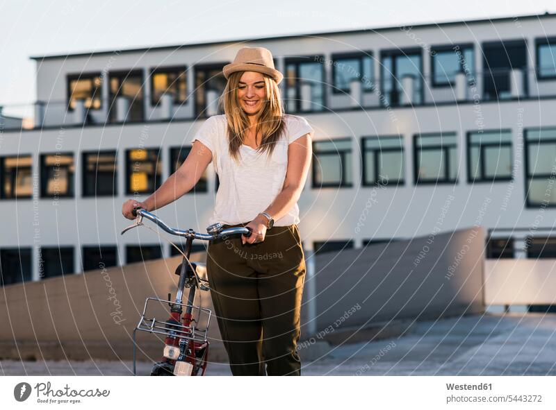 Lächelnde junge Frau mit Fahrrad auf Parkebene weiblich Frauen lächeln Bikes Fahrräder Räder Rad Parkdeck Parkdecks Erwachsener erwachsen Mensch Menschen Leute