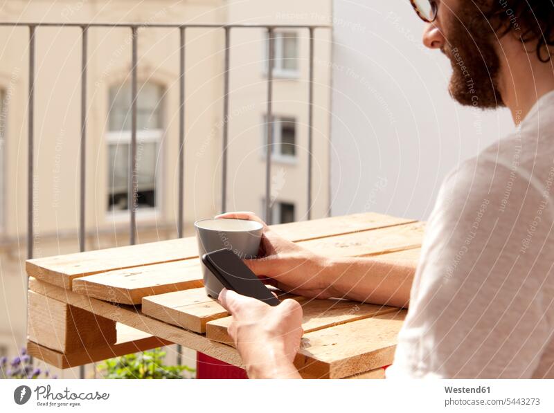 Mann sitzt mit Kaffeetasse auf dem Balkon und telefoniert Balkone Männer männlich Smartphone iPhone Smartphones Erwachsener erwachsen Mensch Menschen Leute