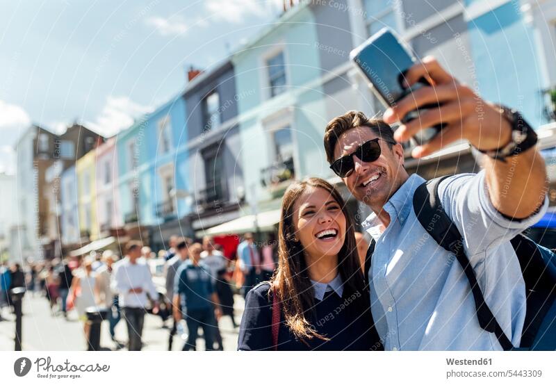 UK, London, Portobello Road, Porträt eines lachenden Paares, das ein Selfie mit einem Smartphone macht Portrait Porträts Portraits Pärchen Partnerschaft Selfies