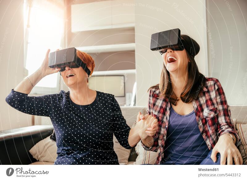 Aufgeregte erwachsene Tochter mit Mutter zu Hause, die eine VR-Brille trägt virtuell Virtualität glücklich Glück glücklich sein glücklichsein Frau weiblich
