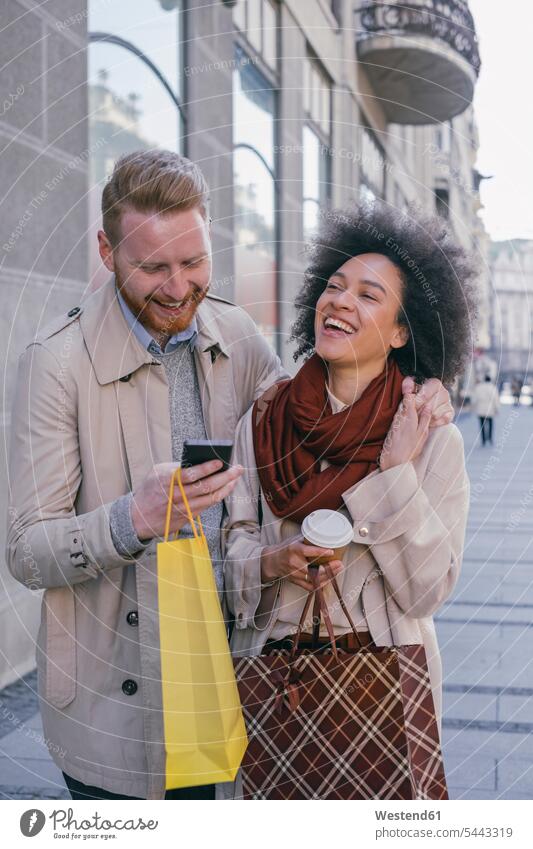 Glückliches Paar in der Stadt mit Handy und Einkaufstaschen Pärchen Paare Partnerschaft lachen Shopping einkaufen shoppen Mobiltelefon Handies Handys
