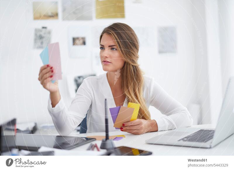 Junge Frau betrachtet Notizen am Schreibtisch im Büro Zettel arbeiten Arbeit Office Büros Arbeitsplatz Arbeitsstätte Arbeitstelle Arbeitstisch Schreibtische
