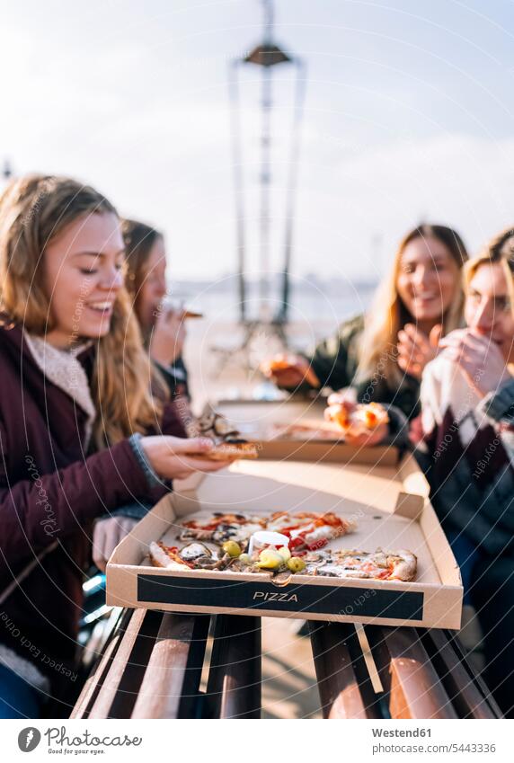 Vier Freunde essen Pizza im Freien Freundinnen Pizzen Freundschaft Kameradschaft Essen Food Food and Drink Lebensmittel Essen und Trinken Nahrungsmittel lächeln