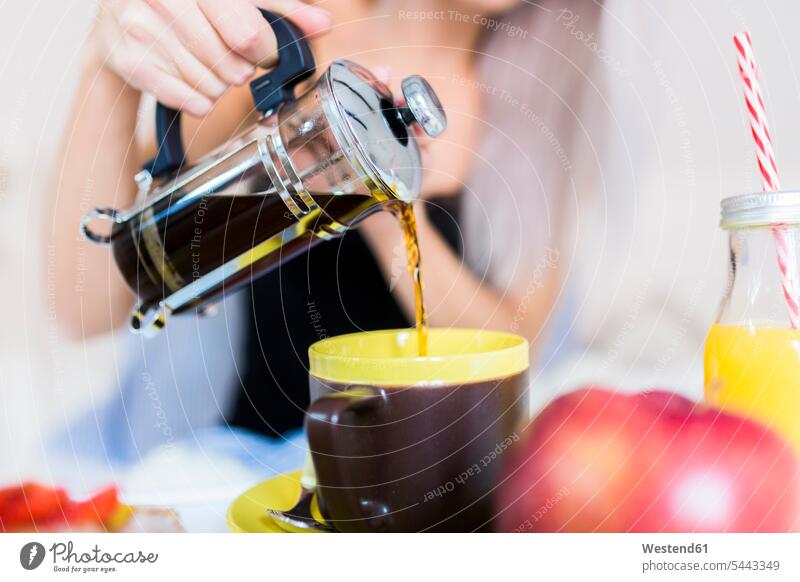 Junge Frau frühstückt im Bett und gießt Kaffee in die Tasse Frühstück frühstücken Betten Tassen eingießen schütten einschenken schuetten weiblich Frauen