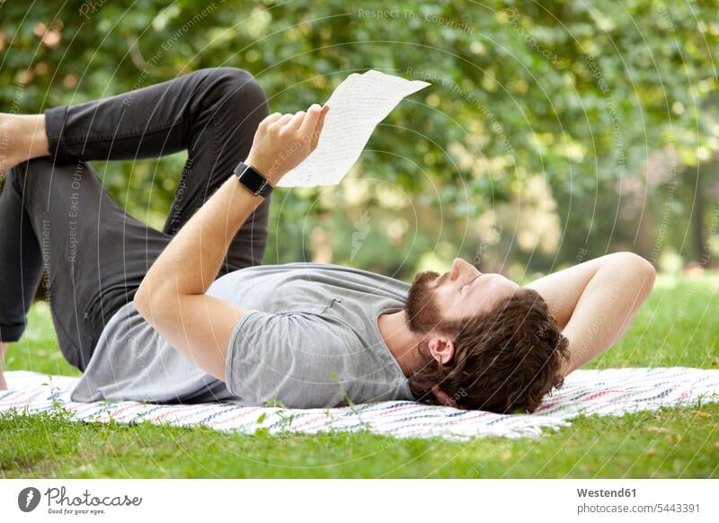Mann liegt auf einer Decke in einem Park und liest einen Brief Briefe Männer männlich Post Nachrichten Erwachsener erwachsen Mensch Menschen Leute People