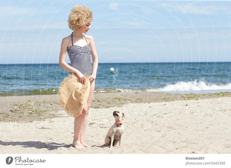 Junge Frau im Badeanzug mit Strohhut und Hund am Strand Hunde weiblich Frauen Beach Straende Strände Beaches Haustier Haustiere Tier Tierwelt Tiere Erwachsener