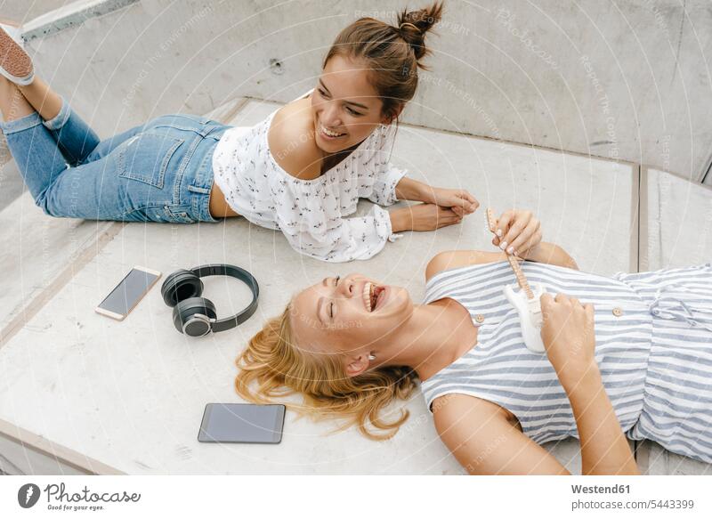 Zwei glückliche junge Frauen liegen auf einer Rampe in einem Skatepark und machen Musik Freundinnen weiblich liegend liegt Skateboardpark Skateboard-Park