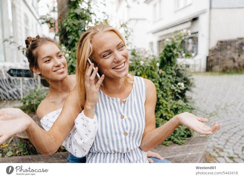 Zwei glückliche junge Frauen mit Handy in der Stadt Freundinnen Mobiltelefon Handies Handys Mobiltelefone staedtisch städtisch Glück glücklich sein