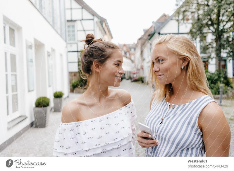 Zwei lächelnde junge Frauen sehen sich in der Stadt an Freundinnen ansehen weiblich staedtisch städtisch Freunde Freundschaft Kameradschaft schauen sehend