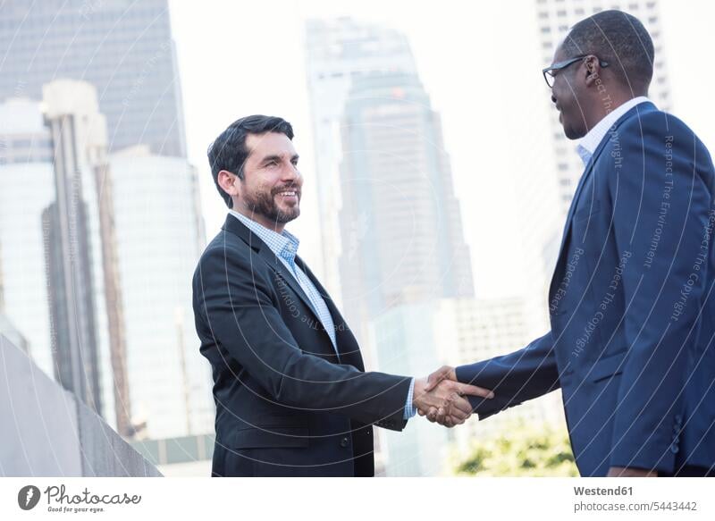 Zwei Geschäftsleute schütteln sich in der Stadt die Hand Handschlag Geschäftsmann Businessmann Businessmänner Geschäftsmänner lächeln Kollegen Arbeitskollegen
