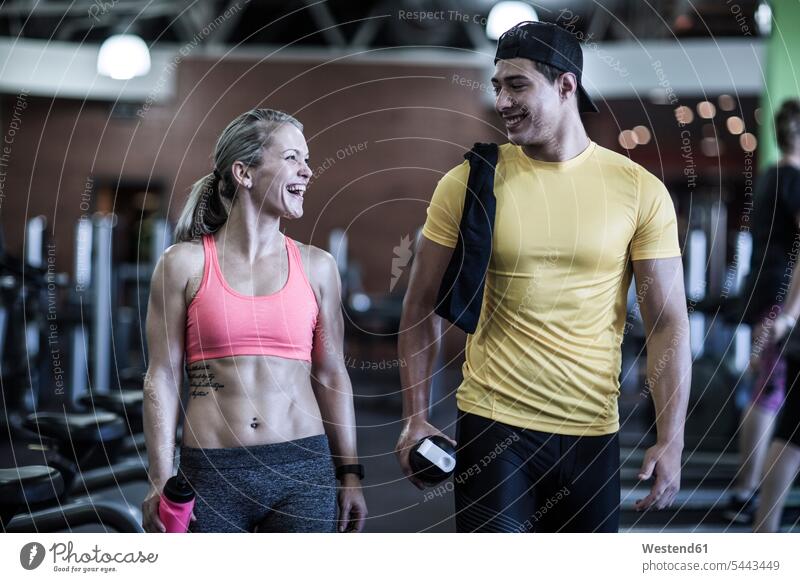 Fröhlicher junger Mann und Frau unterhalten sich im Fitnessstudio lachen Fitnessclubs Fitnessstudios Turnhalle trainieren lächeln positiv Emotion Gefühl