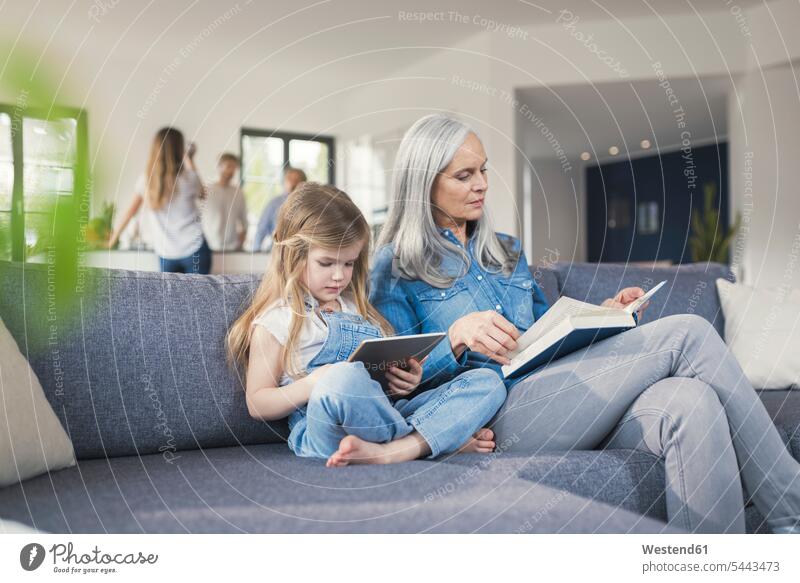 Grossmutter und Enkelin sitzen auf der Couch und lesen gemeinsam Buch und Tablett pc Bücher lernen Lektüre Sofa Couches Liege Sofas Enkeltochter Enkelinnen