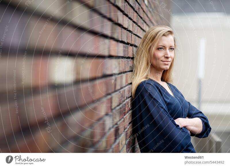 Porträt einer lächelnden blonden jungen Frau, die an einer Ziegelmauer lehnt weiblich Frauen Portrait Porträts Portraits Erwachsener erwachsen Mensch Menschen