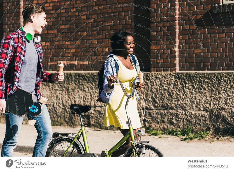 Junges Paar mit Fahrrad und Skateboard auf der Straße Strassen Straßen jung Bikes Fahrräder Räder Rad multikulturell Pärchen Paare Partnerschaft Rollbretter