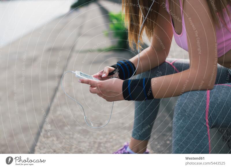 Nahaufnahme einer sportlichen Frau mit Handy und Kopfhörern Mobiltelefon Handies Handys Mobiltelefone trainieren sitzen sitzend sitzt Pause weiblich Frauen