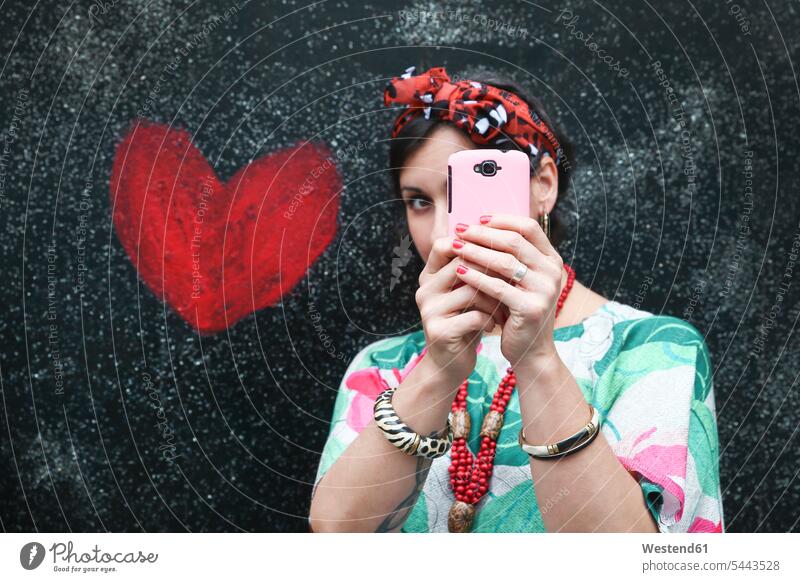 Frau macht ein Selfie neben einem an die Wand gemalten Herz Handy Mobiltelefon Handies Handys Mobiltelefone weiblich Frauen Telefon telefonieren Kommunikation