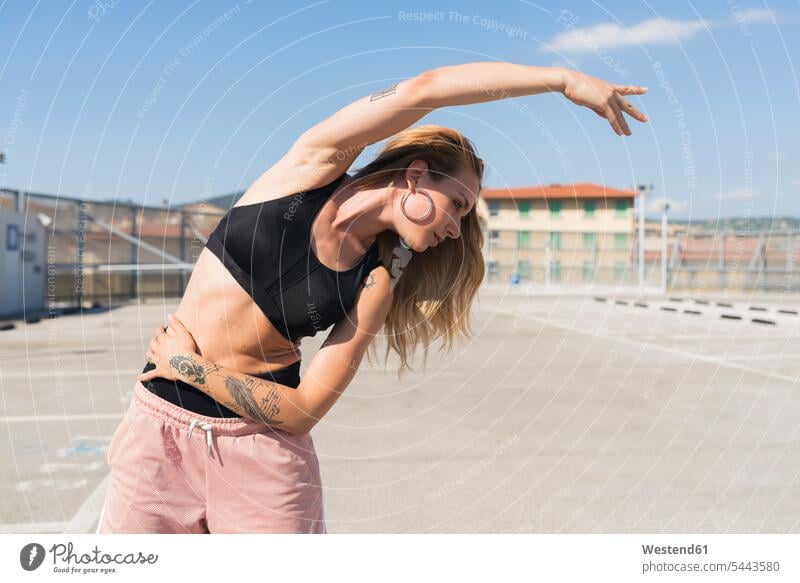 Tätowierte junge Frau macht Dehnungsübungen Stretching dehnen strecken stretchen weiblich Frauen Beweglichkeit Biegsamkeit beweglich Erwachsener erwachsen