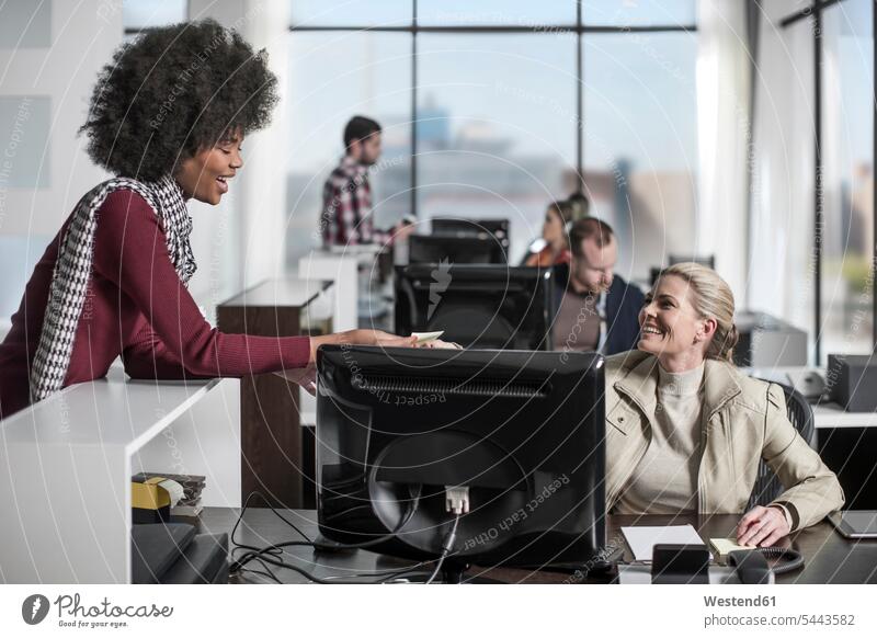 Gelegenheitsbüroangestellte, die hinter dem Schreibtisch am Computer Notizen an einen Kollegen übergibt Kollegin Kolleginnen lächeln Büro Office Büros