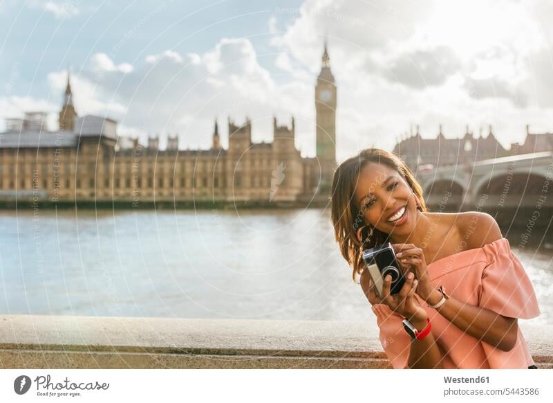 UK, London, glückliche Frau hält eine Kamera in der Nähe der Westminster Bridge Fotoapparat Fotokamera lachen weiblich Frauen positiv Emotion Gefühl Empfindung