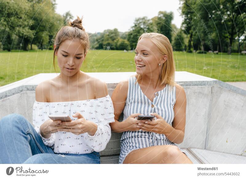 Zwei glückliche junge Frauen mit Mobiltelefonen in einem Skatepark Freundinnen Skateboardpark Skateboard-Park Skateboard Park Skaterplatz Parkanlagen Parks
