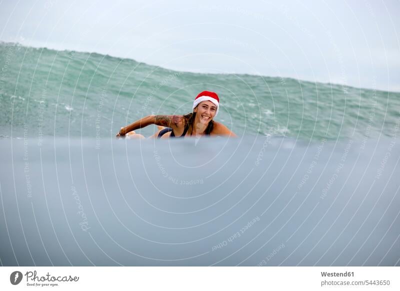 Indonesien, Bali, lächelnde Frau auf dem Surfbrett mit Weihnachtsmannmütze Surfbretter surfboard surfboards Welle Wellen Meer Meere Surfen Surfing Wellenreiten