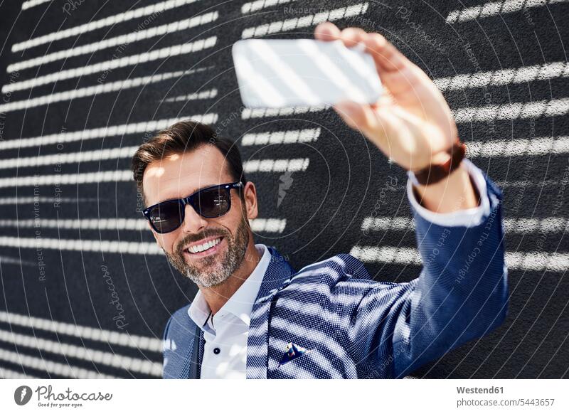 Geschäftsmann macht Selfie mit Smartphone im Freien Selfies Handy Mobiltelefon Handies Handys Mobiltelefone Businessmann Businessmänner Geschäftsmänner lächeln