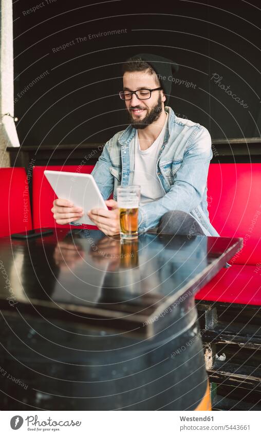 Lächelnder junger Mann sitzt in einer Kneipe und benutzt Tabletten Tablet Computer Tablet-PC Tablet PC iPad Tablet-Computer Kneipen Männer männlich Rechner