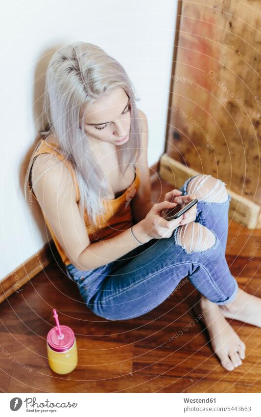 Junge Frau sitzt zu Hause auf dem Boden und benutzt ein Smartphone Zuhause daheim benutzen sitzen sitzend weiblich Frauen Böden Boeden iPhone Smartphones