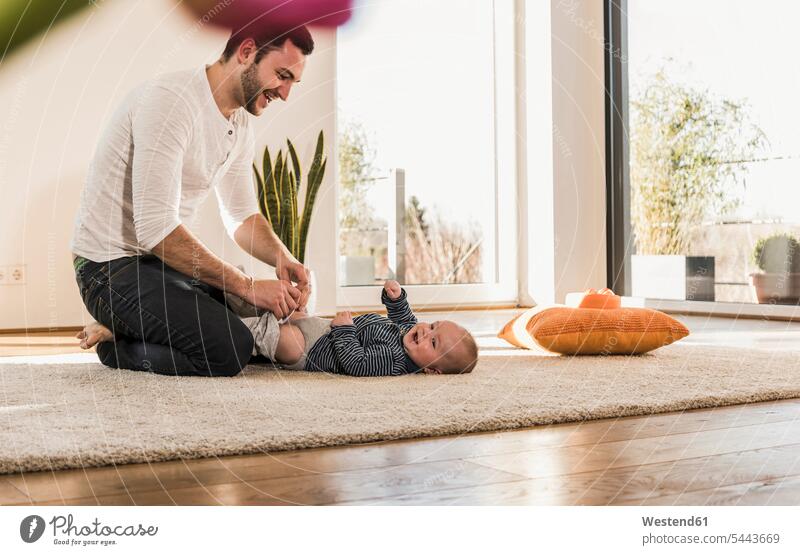 Vater wechselt Windeln und spielt mit seinem kleinen Sohn Papas Väter Vati Vatis Papis knuddeln umarmen lachen spielen Kind Babies Babys Kinder Zuhause zu Hause