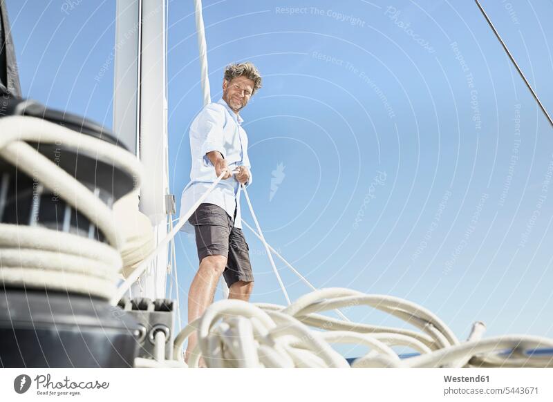 Lächelnder reifer Mann arbeitet mit Seilen auf einem Segelboot Männer männlich Segeln segelnd segelt Erwachsener erwachsen Mensch Menschen Leute People Personen