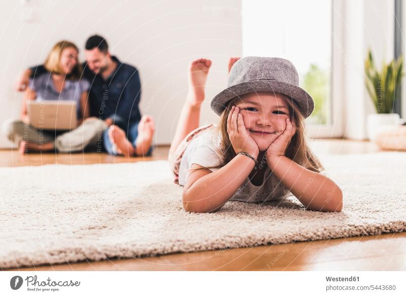Kleines Mädchen mit Hut amüsiert sich zu Hause, Eltern mit Laptop im Hintergrund Deutschland Quality Time Wohnen Gemeinsamkeit zusammen gemeinsam