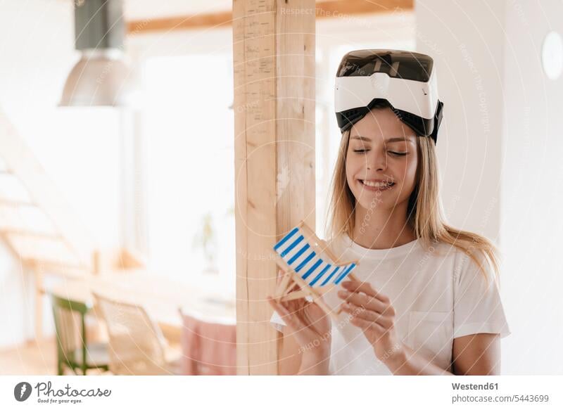 Junge Frau trägt VR-Brille, plant Urlaub, hält Spielzeugstuhl Planung Pläne planen Ferien Loft Lofts Virtual Reality Brille Virtual-Reality-Brille
