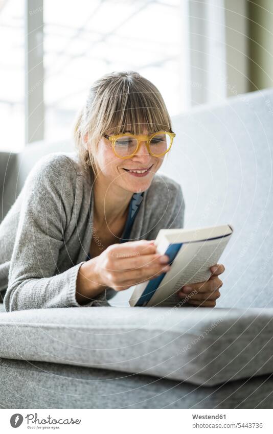 Lächelnde Frau liegt auf Couch und liest Buch Bücher weiblich Frauen liegen liegend lächeln Sofa Couches Liege Sofas Erwachsener erwachsen Mensch Menschen Leute